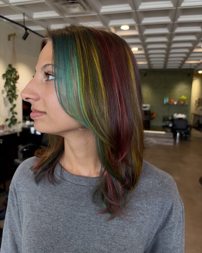 Client in profile with a shoulder-length cut and red, yellow, and green vivid highlights